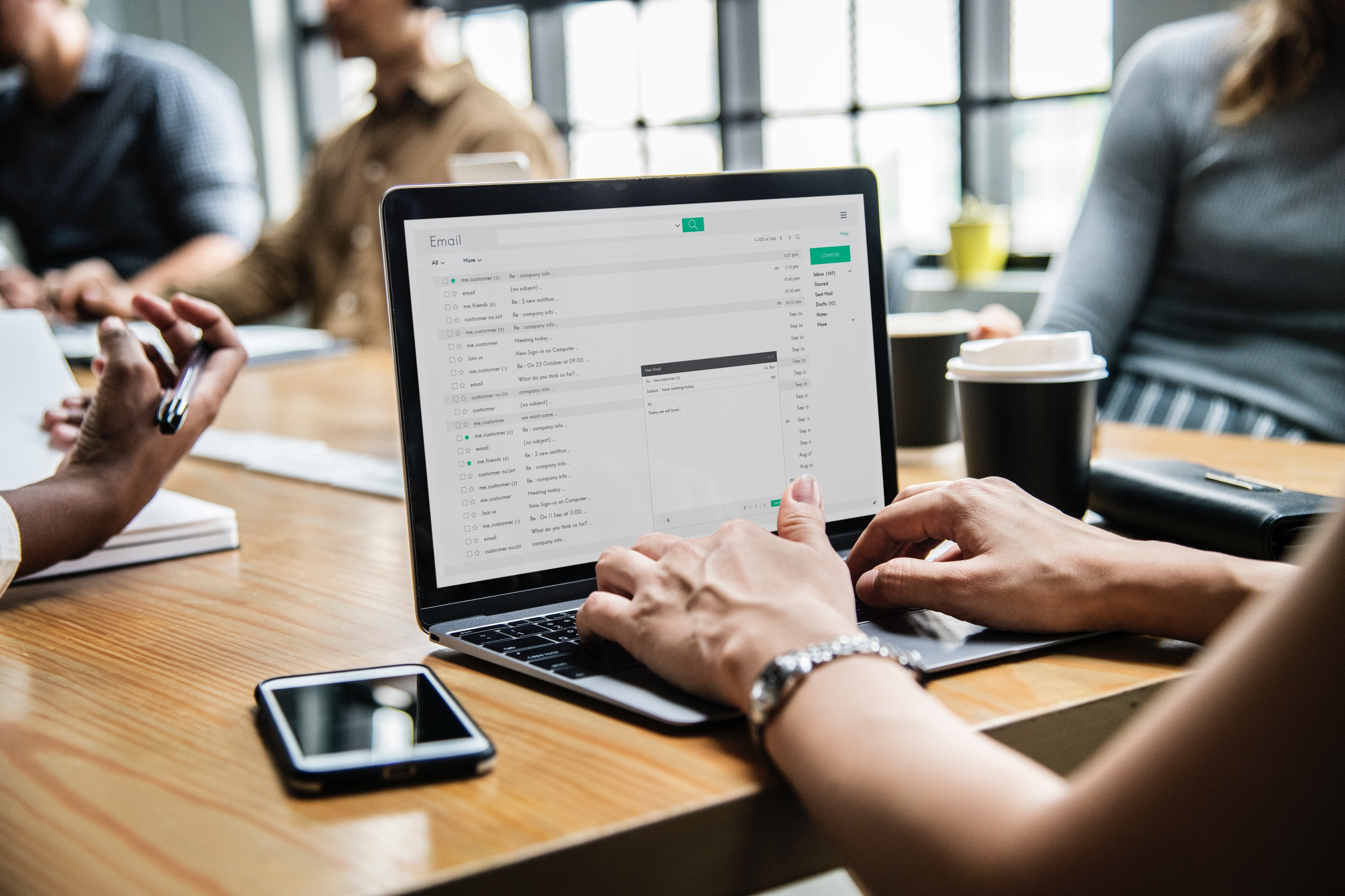 arms-of-person-out-of-frame-typing-on-laptop-email-at-conference-table-with-coworkers